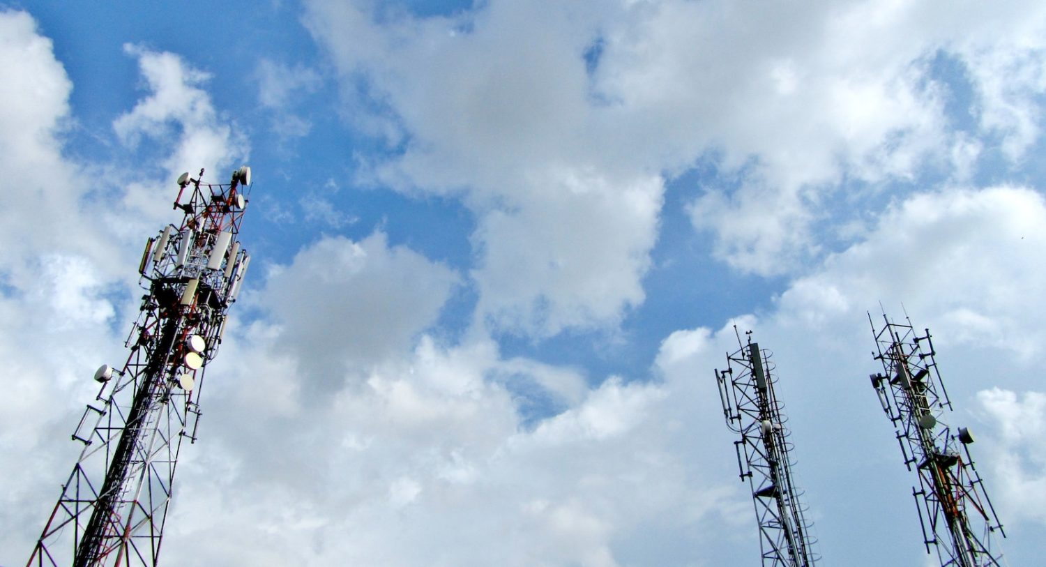 a group of cell towers sitting under a cloudy blue sky