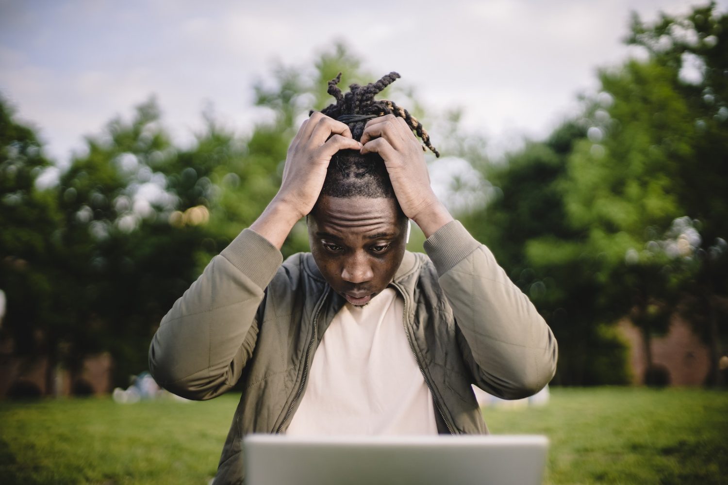 Upset young African American male freelancer clutching head with hands after failure in project while working remotely in park